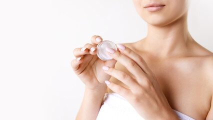 Cropped image of woman in towel after shower against white studio background. Holding little bottle of under eye cream. Concept of female beauty, skin care, cosmetology and cosmetics, health, ad