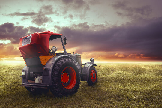 alter traktor von einem bauern auf  grüner wiese bei schönen sonnenuntergang im abendrot