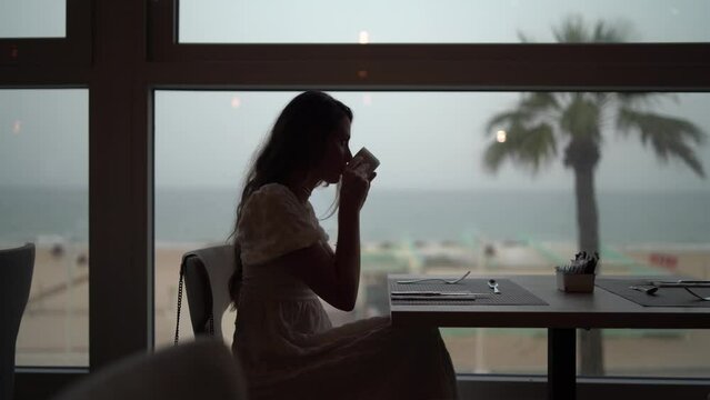 Chica joven en cafeter&iacute;a restaurante de hotel de lujo tomando bebida caliente mirando por la ventana y visitando el establecimiento