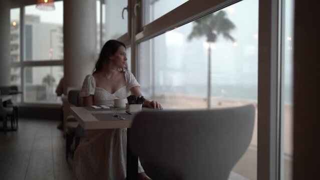 Chica joven en cafeter&iacute;a restaurante de hotel de lujo tomando bebida caliente mirando por la ventana y visitando el establecimiento