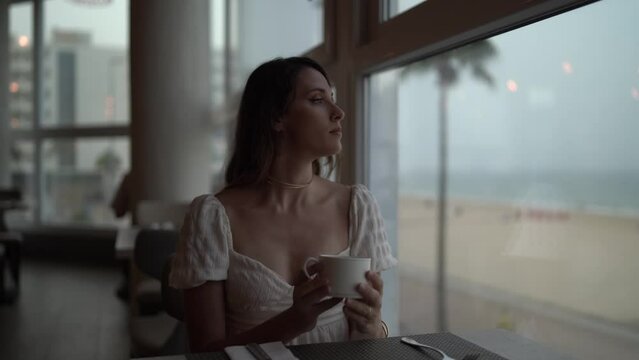 Chica joven en cafeter&iacute;a restaurante de hotel de lujo tomando bebida caliente mirando por la ventana y visitando el establecimiento