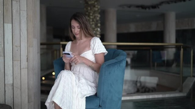 Toma en 4k de chica sentada en hall de hotel chateando por el smartphone