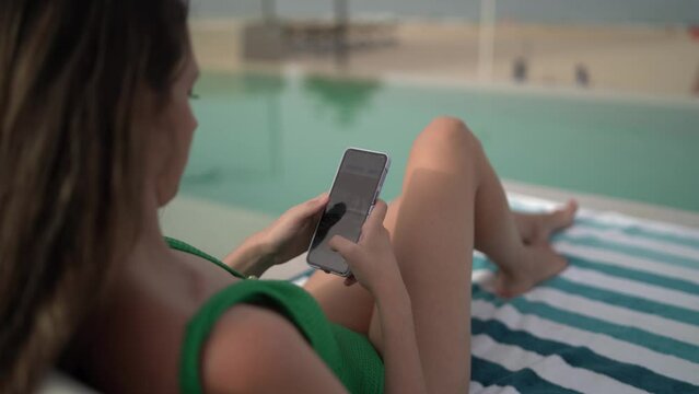 Plano cerrado de las manos de una chica tumbada en la piscina de un hotel con el smartphone