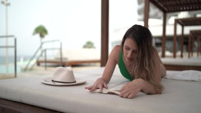 Chica joven en hamaca de piscina de hotel leyendo y disfrutando de las vacaciones