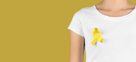 Woman with golden awareness ribbon on yellow background with space for text. Cancer concept