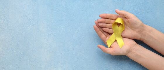 Hand with yellow awareness ribbon on light blue background with space for text. Cancer concept