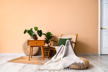 Cozy armchair with cushion, plaid, houseplants and table near beige wall