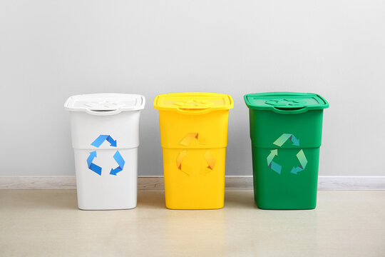 Different garbage bins with recycling symbol near white wall