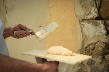 A worker applies a finishing coat to a stone wall with a trowel to begin construction.