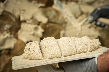 A worker applies a product to a stone wall with a trowel to begin construction.
