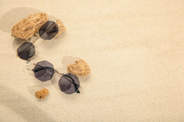 Fototapeta na wymiar Stones with stylish sunglasses on sand