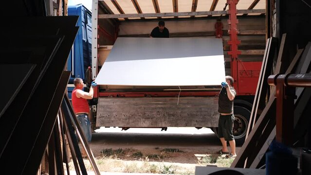 truck for transportation. Men unload a sheet of hardboard