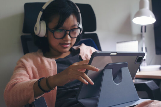 Asian children using digital tablet with stylus pen write and do homework at home. Happy Thai Student working online and use headphone to study for the exam. Education and E-learning concept.