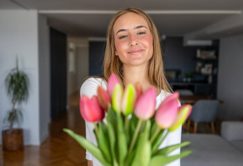 Single smiling gorgeous young adult woman with tulip bouquet at home