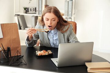 Happy young woman eating sushi with laptop in office