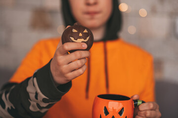 Portrait of candid authentic zoomer boy posing with jack lantern mug and sweets at halloween party
