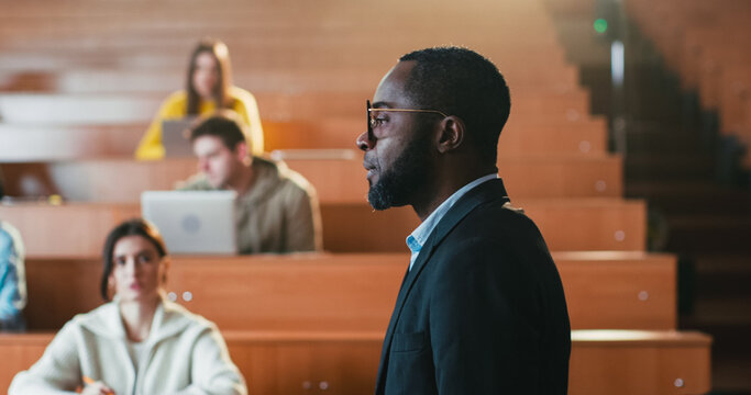 Afican American male professor standing and walking in front of students and giving lection. Man teacher explaining lesson subject in auditorium. Close up. Teaching work. Working at University.
