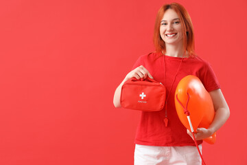 Female lifeguard with rescue buoy and first aid kit on red background