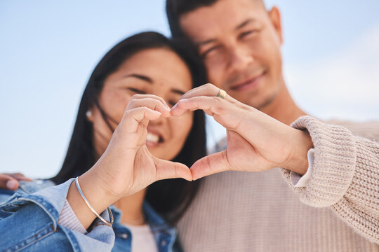 Love, heart hands and portrait of happy couple with blue sky, nature and holiday travel for summer. Care, marriage and smile, loving sign language emoji with man and woman on beach vacation together. - Powered by Adobe
