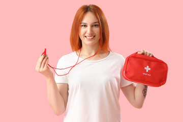 Female lifeguard with whistle and first aid kit on pink background