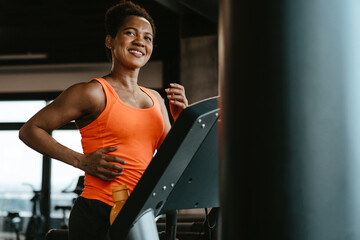 Beautiful motivated young woman in orange sportswear running on a treadmill in the fitness gym with...