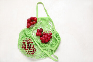 Mesh bag with fresh grapes on white background