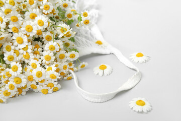 Mesh bag with beautiful chamomile flowers on white background, closeup
