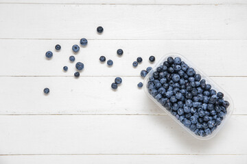 Plastic container with fresh blueberry on light wooden background