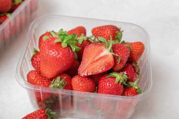 Plastic container with fresh strawberry on light background, closeup
