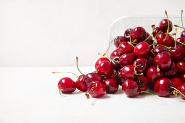 Plastic container with fresh cherry on light background, closeup