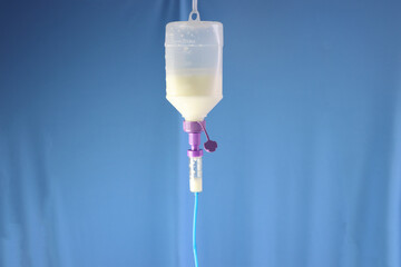 Enteral nutrition diet bottle hanging and infusing enteral diet throughout an infusion set. Blue background - obrazy, fototapety, plakaty
