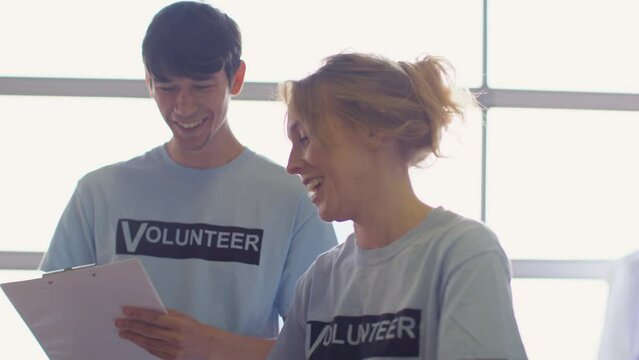 Male and female charity workers sorting through donations of clothing to thrift store - shot in slow motion