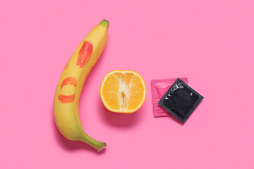 Fresh banana with lipstick kiss, orange and condoms on pink background. Sex education concept