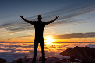 Fototapeta premium silhouette of man standing and spread hand on the top of mountain to enjoy colourful sky