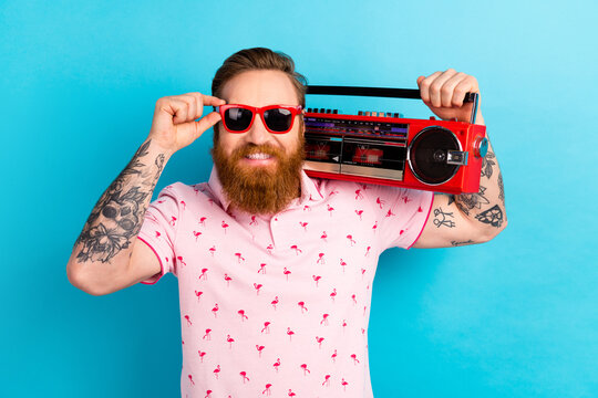 Photo of optimistic glad man wear trendy pink clothes hold radio listen music 90s isolated on blue color background
