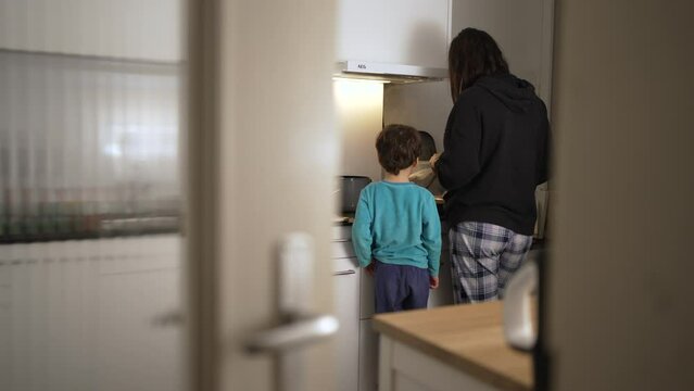 Mother and Child in Kitchen Through Door Crack at Night. Peeking at Nighttime Kitchen Moments of Mother and Son preparing food