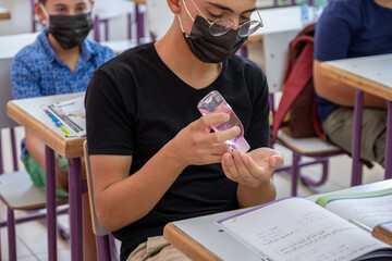 Teenager in school sterilizing his hands while wearing face mask to prevent infection