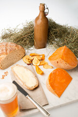 Mimolette Käse mit Brot, Butter, Bier und Gemüsechips an Heu