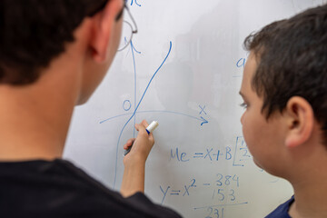 Two students are studying together using the whiteboard in school