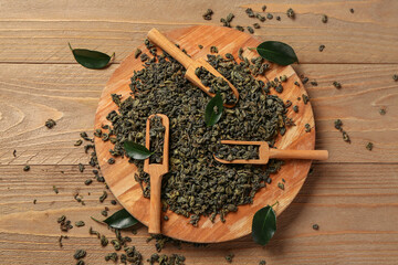 Board with scoops and green tea leaves on wooden background