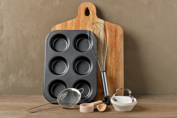 Set of baking utensils on wooden table near brown wall