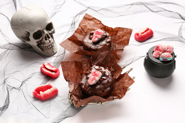 Composition with delicious chocolate cakes with candies and skull for Halloween celebration on white background, closeup