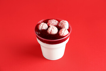 Plastic cup with delicious panna cotta with candies for Halloween celebration on red background