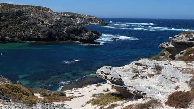 Water splashing on the cliffs of Rottnest Island, Western Australia. Beautiful wild and rocky landscape of Rottnest Island. Dark blue sea around rocky cliffs. Sunny day on Australian island.