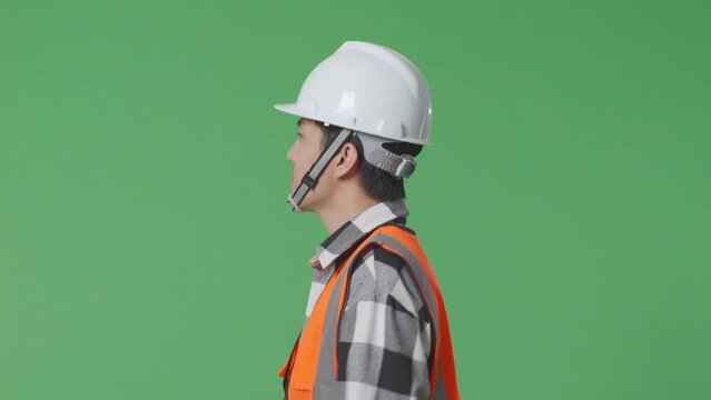 Close Up Of Side View Asian Male Engineer With Safety Helmet Waving Hand While Walking In The Green Screen Background Studio
