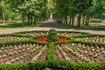 Round flower bed and alley in the city garden on a sunny summer day