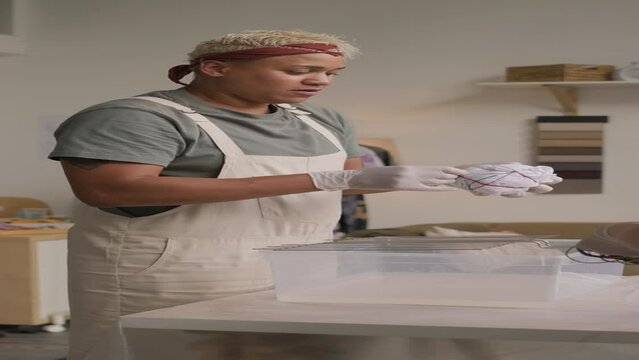 Vertical medium shot of Biracial female fashion designer making tie dye print on white t-shirt while working with colleague in creative space at daytime