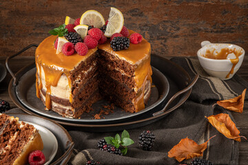 Delicious semi-naked chocolate cake with caramel topping and decorated with blackberries and raspberries. Dark background