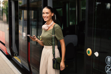 Joyful Passenger Young Lady Exiting Tram, Texting on Phone - obrazy, fototapety, plakaty