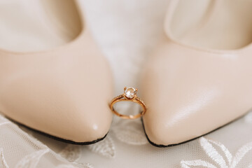 Beige elegant shoes. A diamond engagement ring sits between a pair of classic wedding shoes. Fashion. Style. Wedding photo